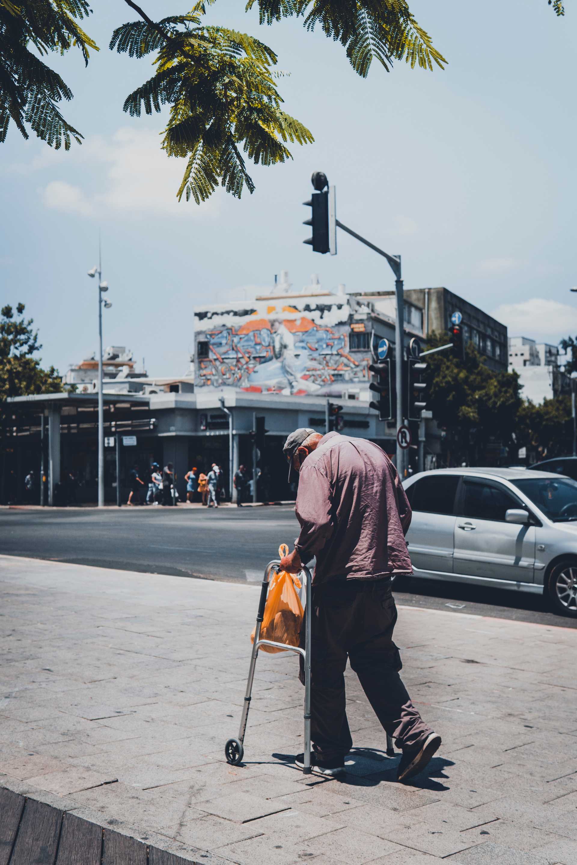 A man with a walker walks across a cracked sidewalk.