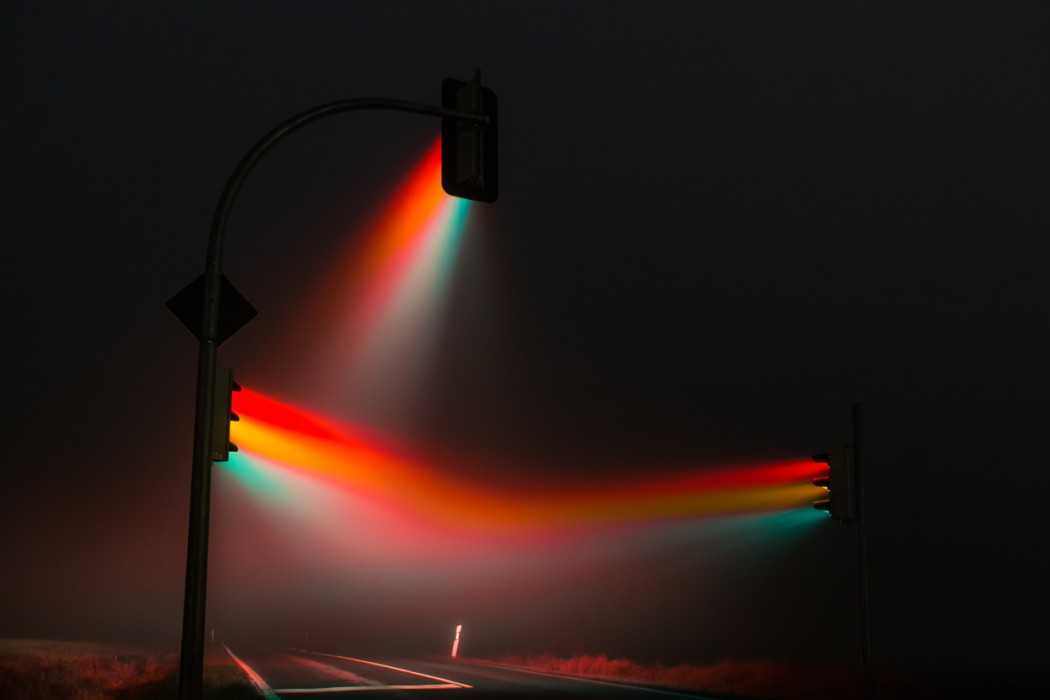 Multi-colored beams radiate from streetlights at night.