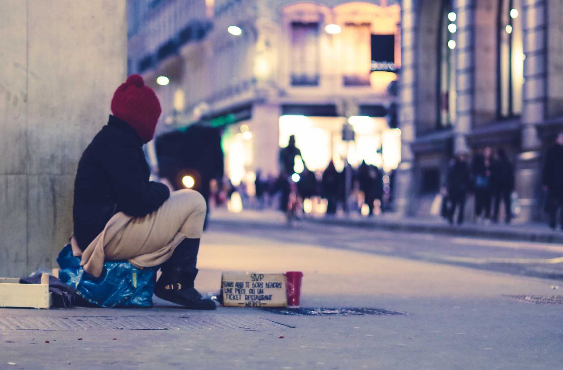 A homeless person sits on a street corner.