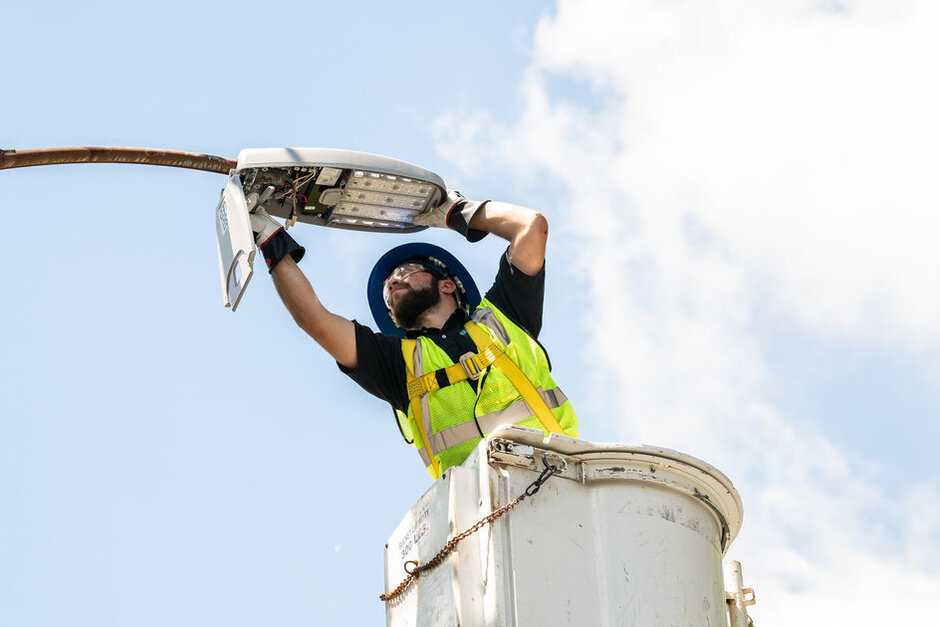 A worker in a bucket lift installs networking equipment on a streetlamp.