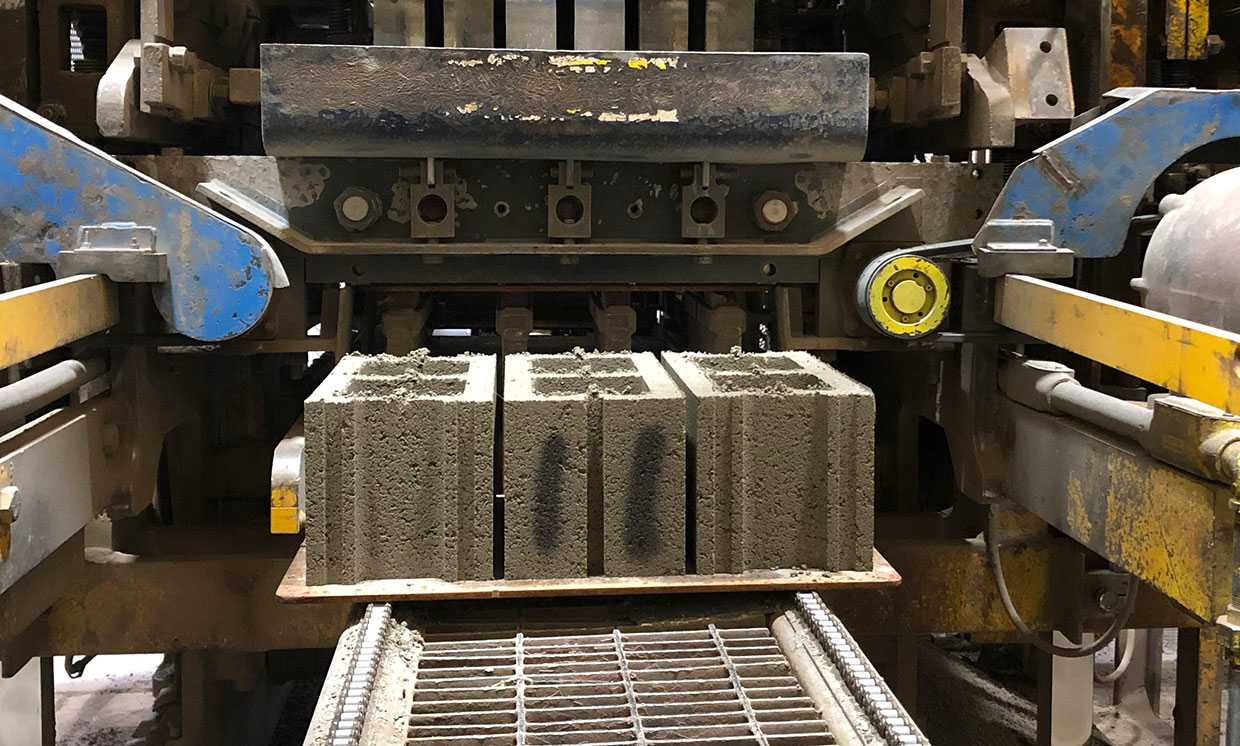 Three cement blocks exit a fabrication machine.