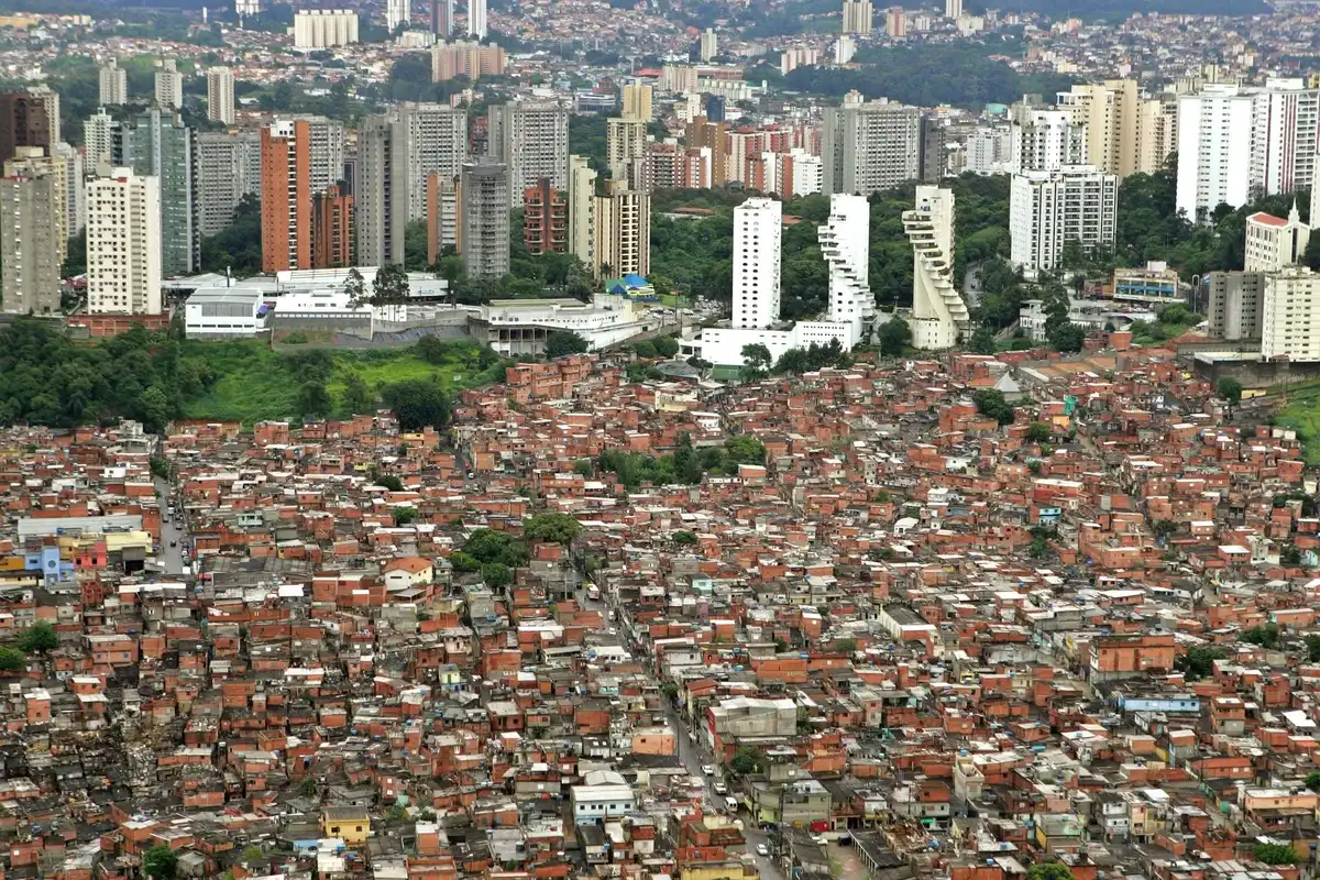 An aerial view of an informal settlement separated from a neighborhood high-rise housing estate by a narrow wall.
