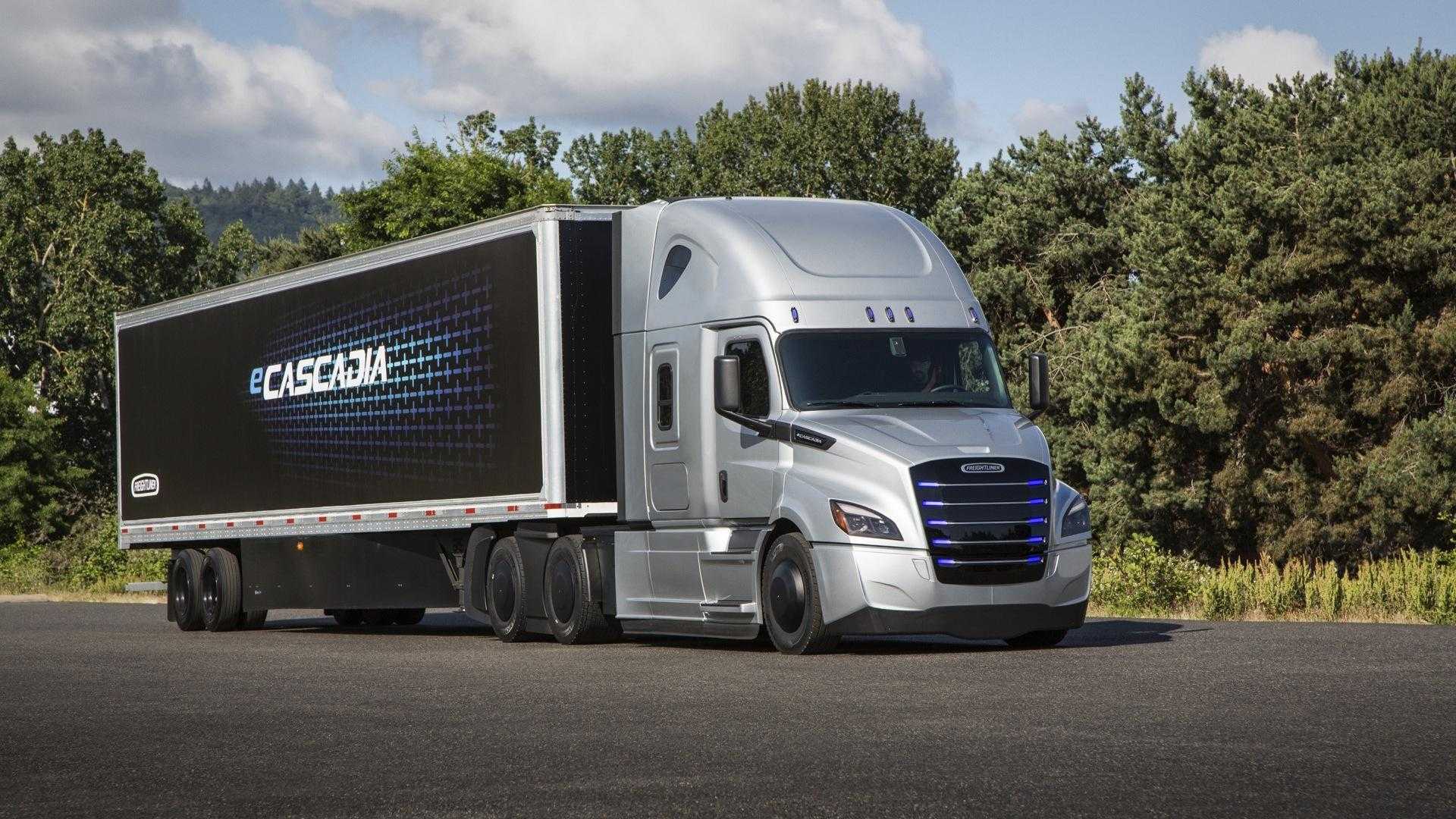 A modern-looking black and silver tractor trailer is parked against a forest.