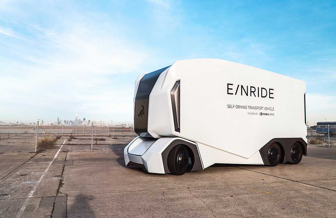 A large while self-driving truck is parked in a vacant lot.