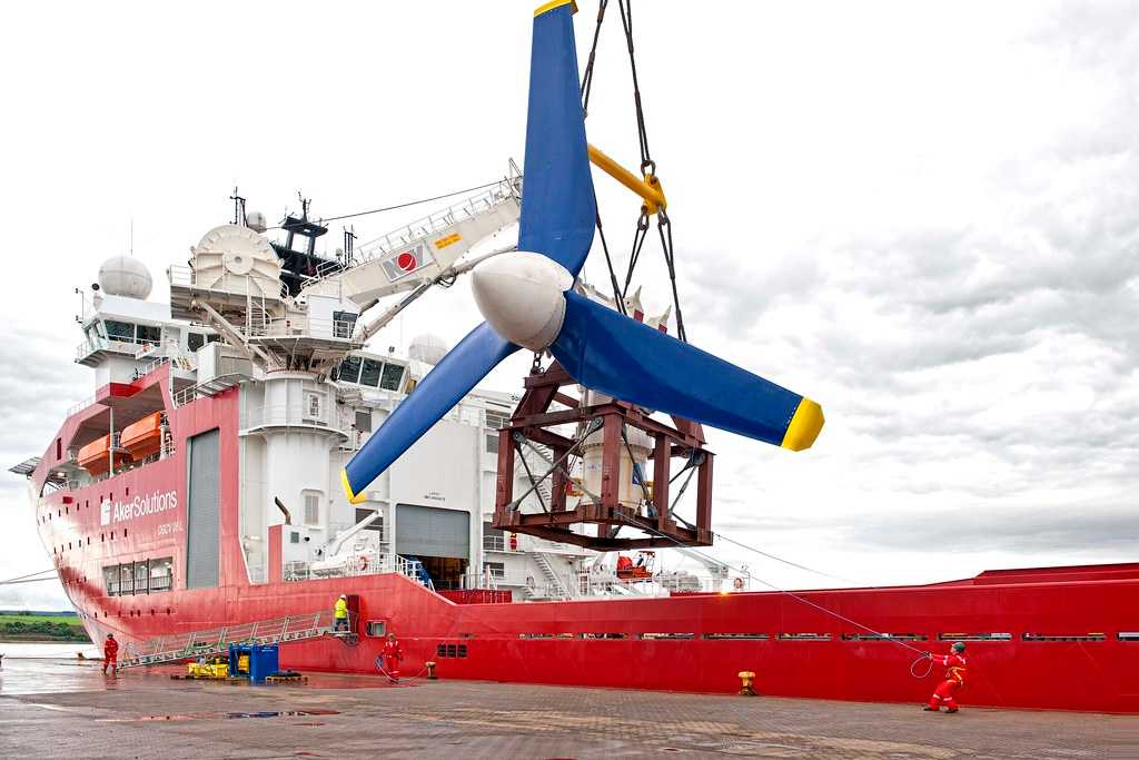 A crane on a ship lowers a large turbine assembly into the water.