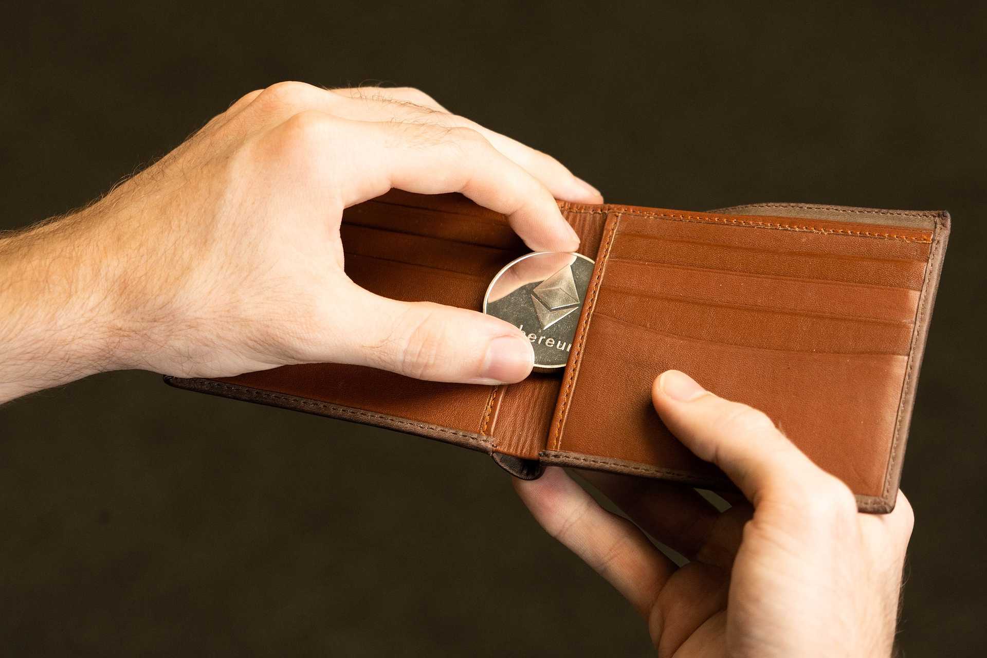  Image showing someone place an Ethereum coin inside a wallet.
