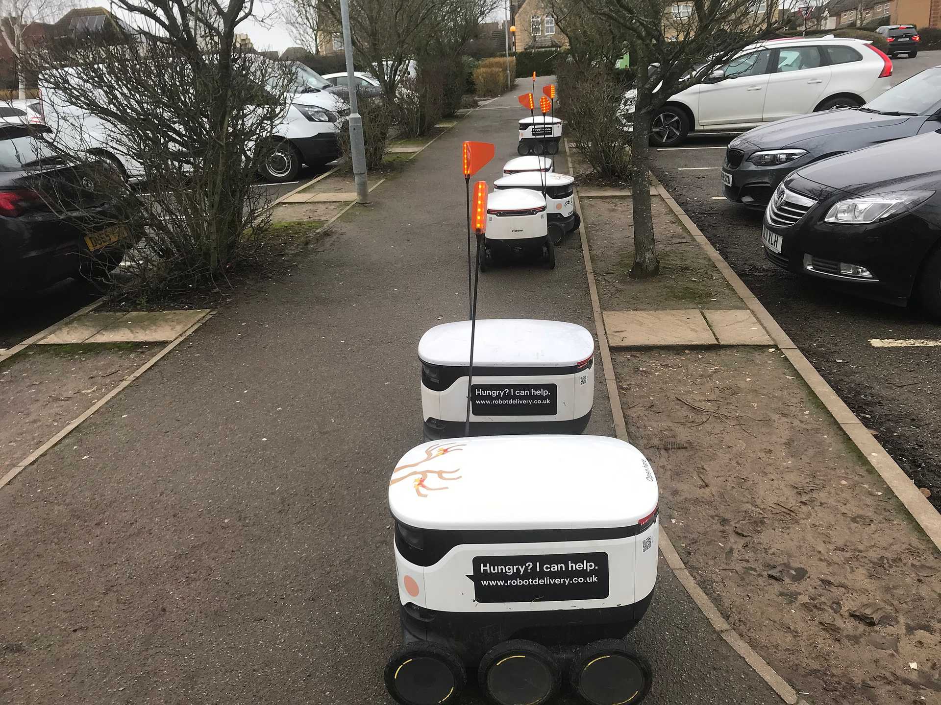 A group of robot delivery carts waits along a pedestrian path.