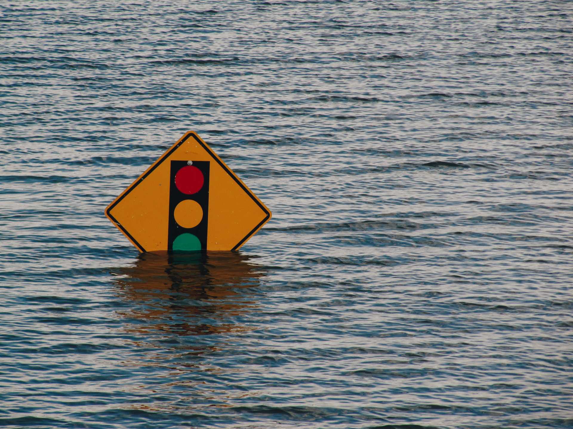 A traffic sign indicating a stop light is half submerged by flood waters.