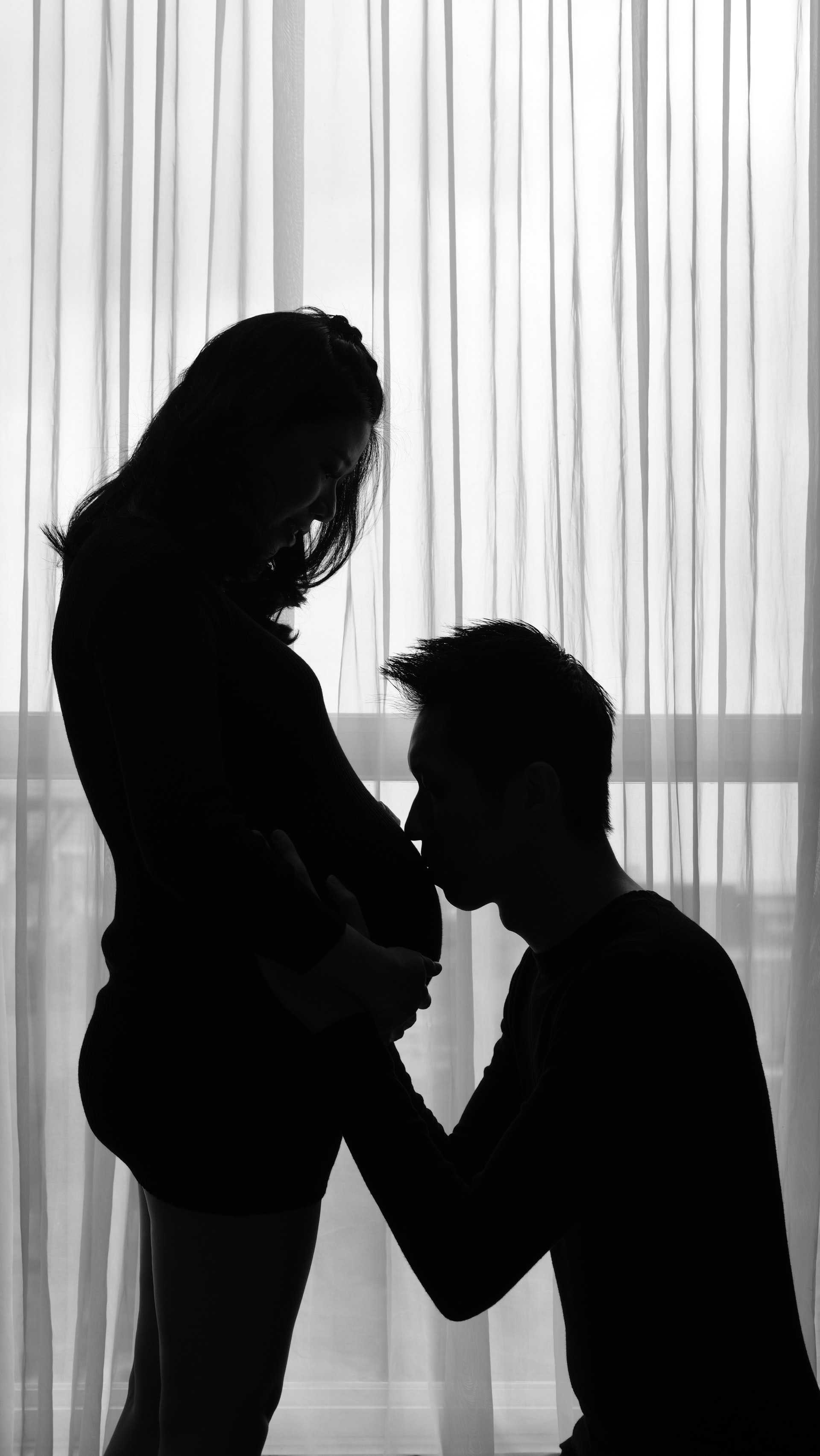 Silhouette of a man kissing the belly of a pregnant woman.