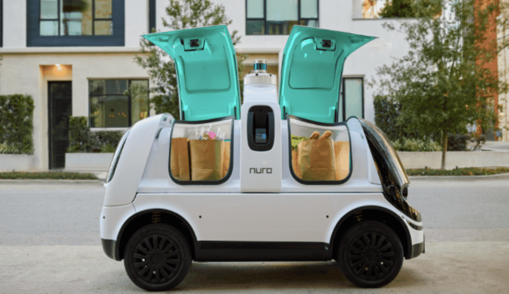 A self-driving delivery vehicle is parked with gull wing doors open to reveal paper bags filled with groceries.