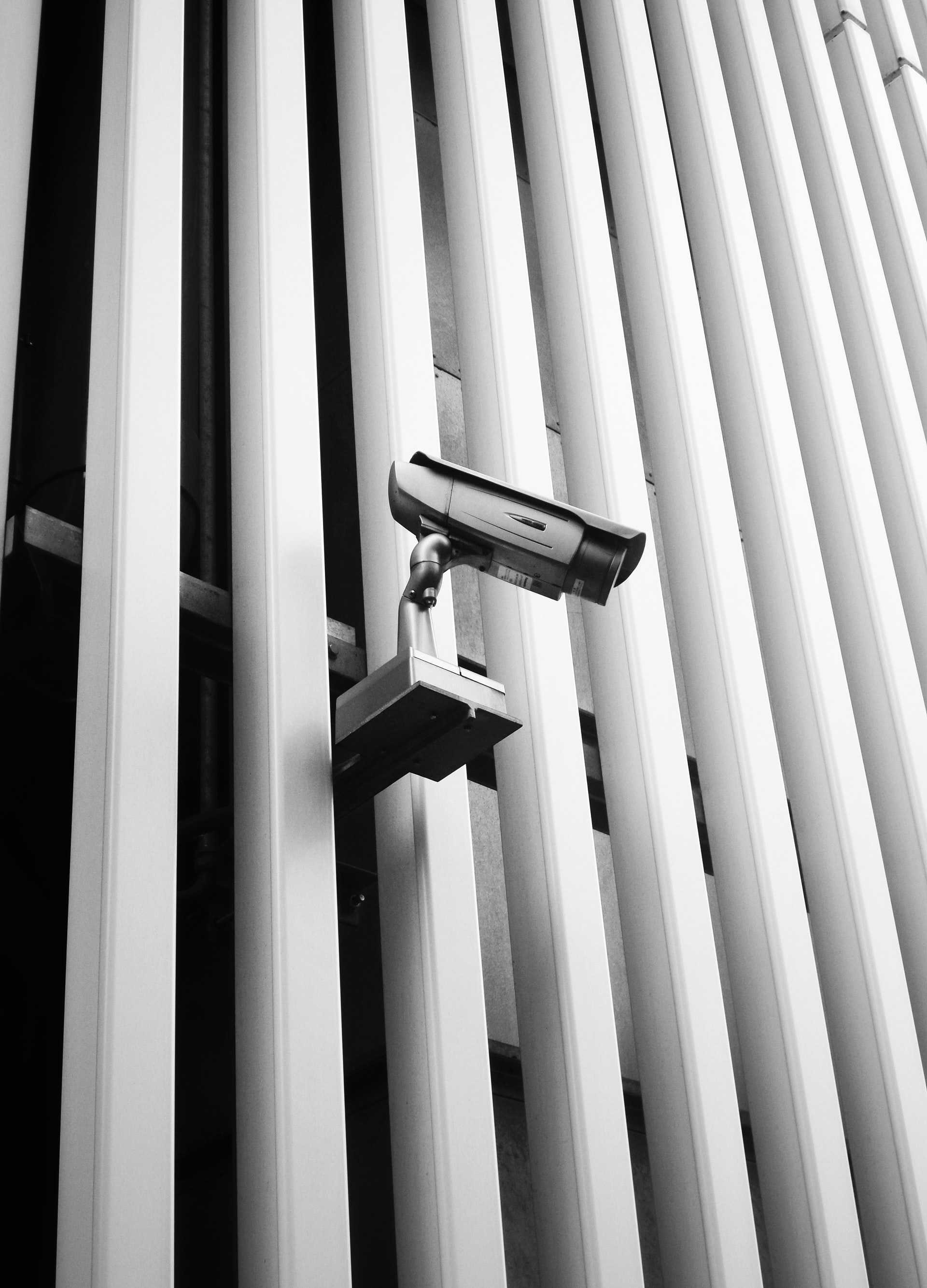 A surveillance camera juts out from a modern office building.
