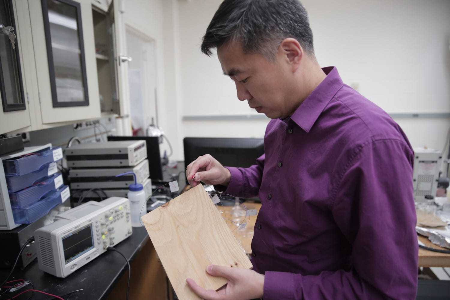 An Asian scientist in a purple shirt examines a piece of flooring material.