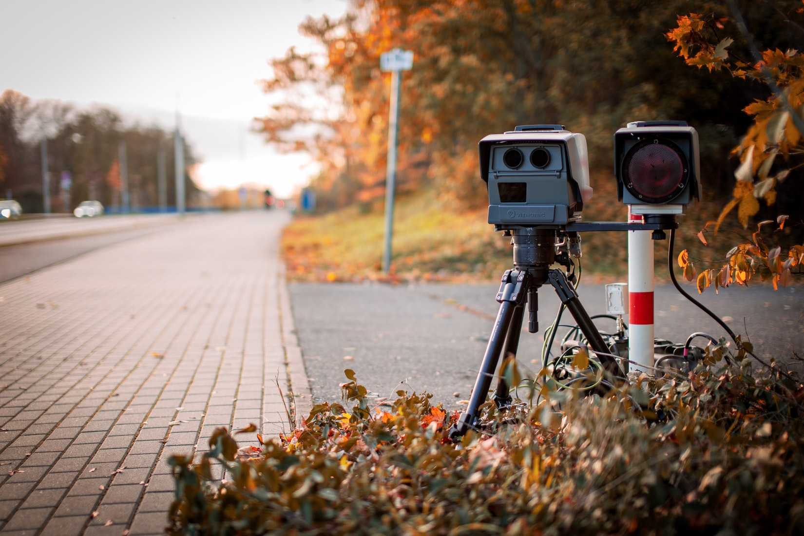 A speed camera mounted by the side of a road.