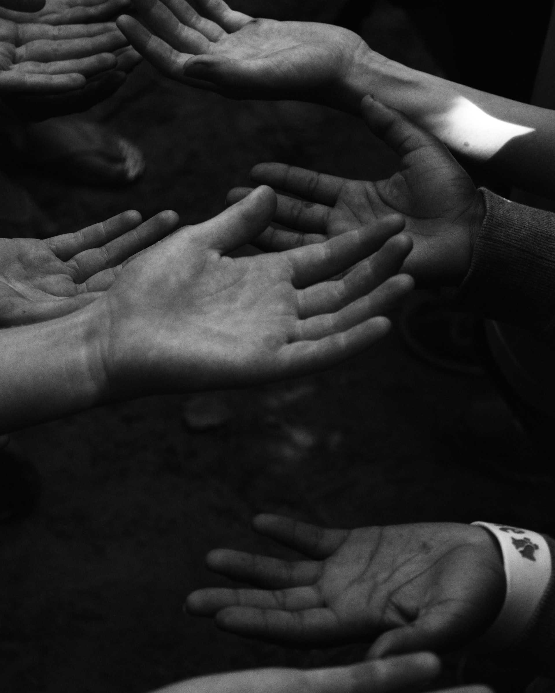 Black and white photo of several upturned, outstretched hands.