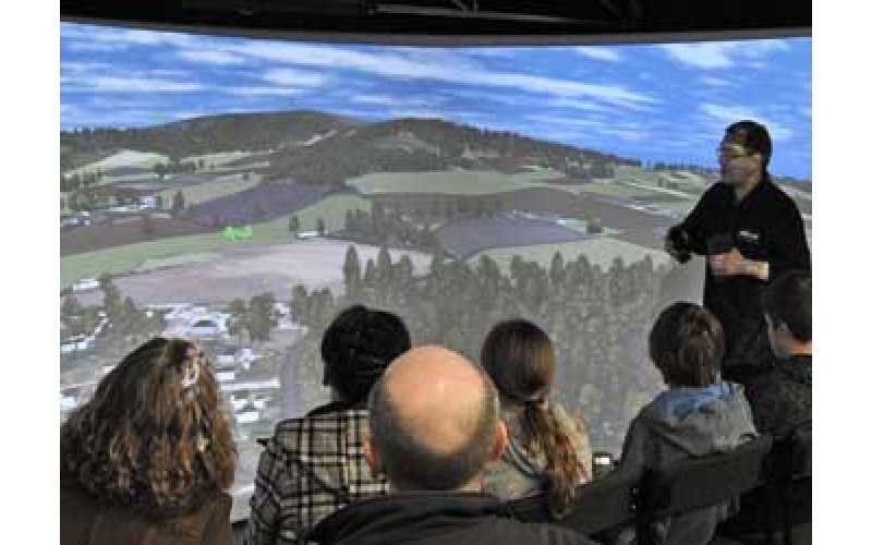 A group of people view a wall-sized projection of a proposed urban plan.