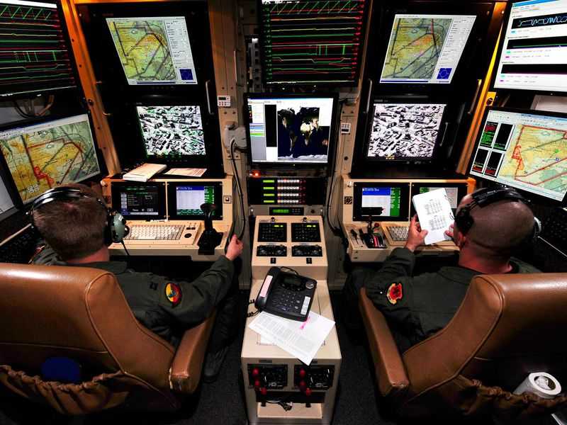 Drone pilots sit at command consoles.