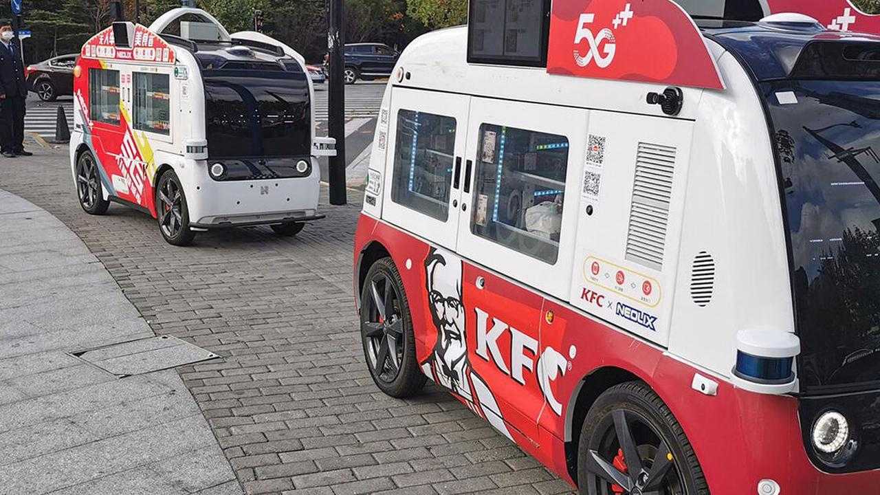 Two red and white self-driving minivans offer food for sale.