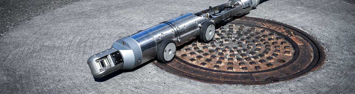 A long cylindrical robot with small wheels sits atop a manhole cover.