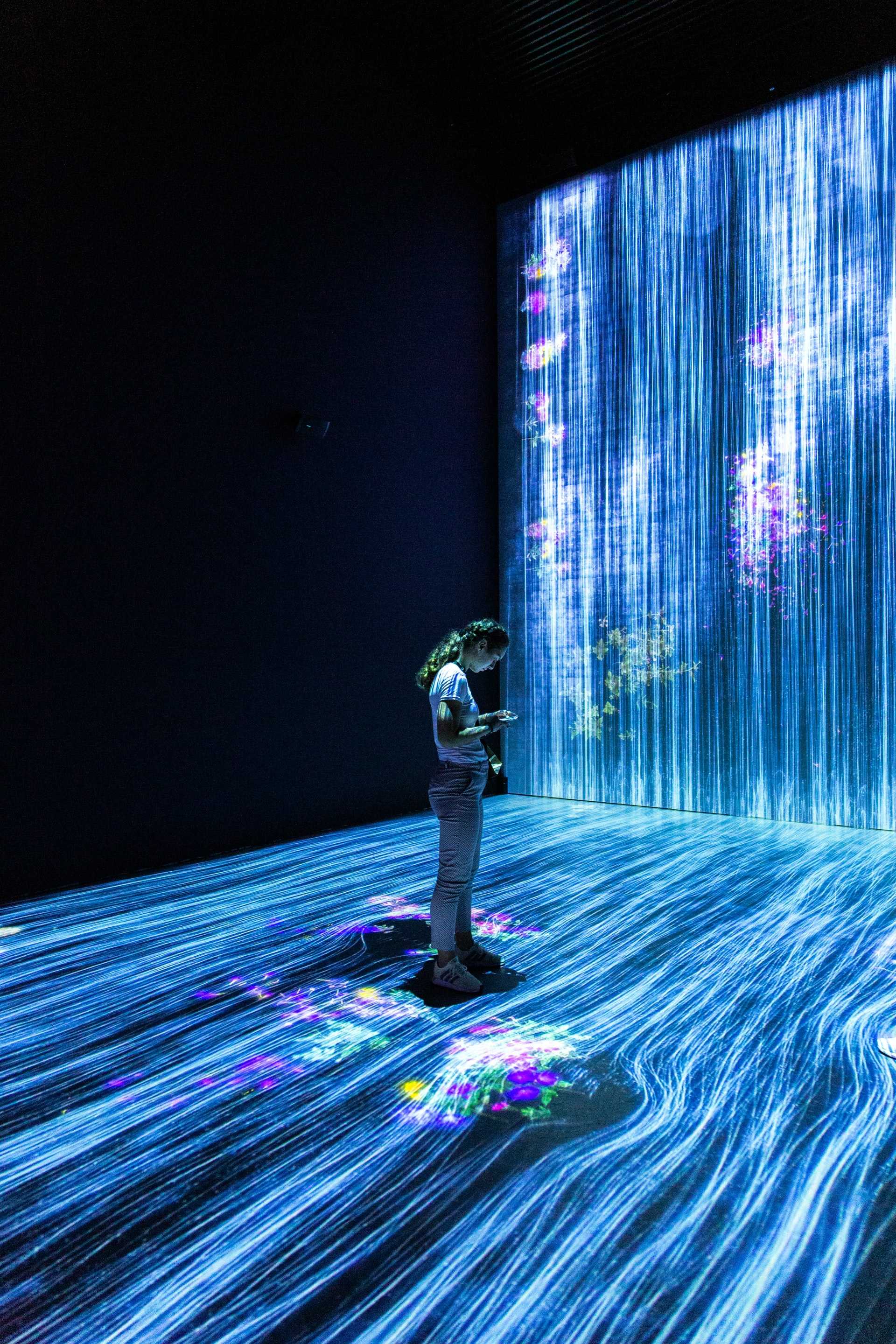 A woman stands in a projected waterfall composed of circuit and data symbols.